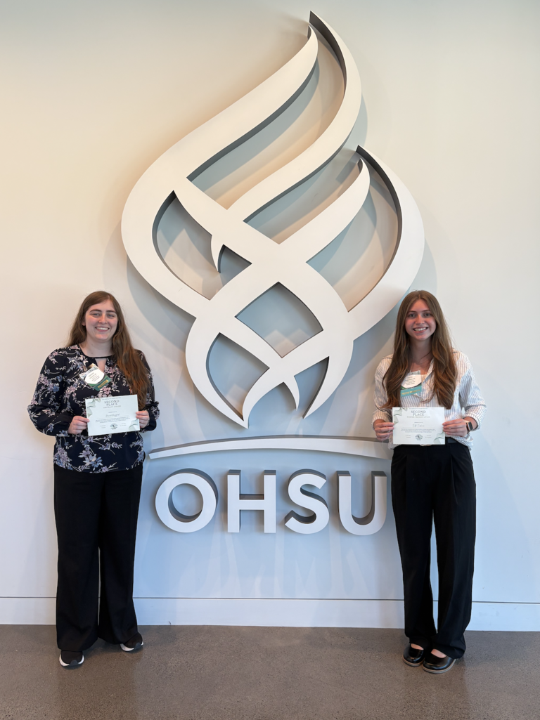 Hannah and Faith holding their awards in front of OHSU logo